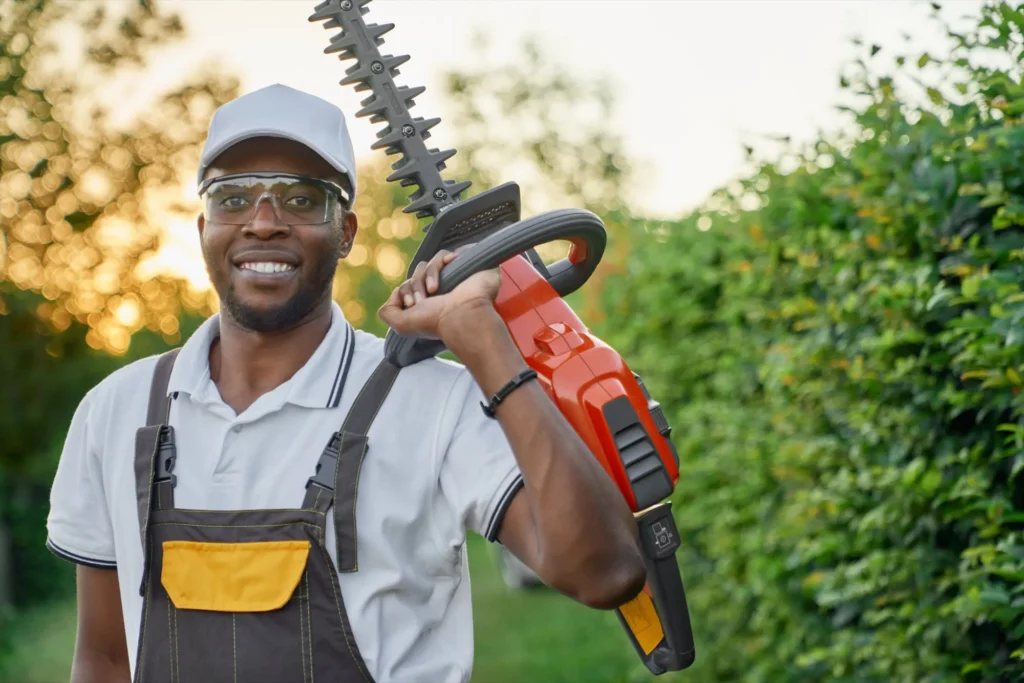 Portrait of smiling afro man in overall with hedge trimmer